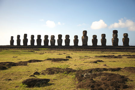 a row of statues in a field with Easter Island in the background