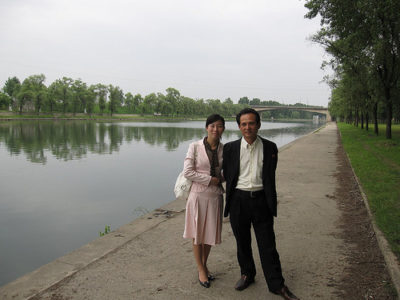 a man and woman standing on a sidewalk next to a body of water