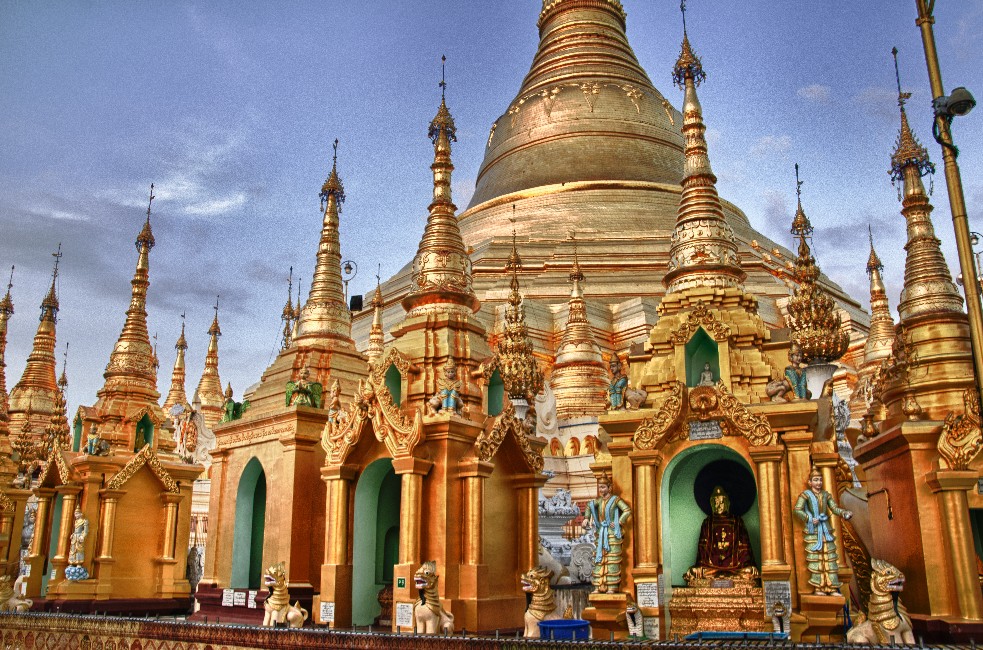 a large gold and gold building with a statue in front of it with Shwedagon Pagoda in the background
