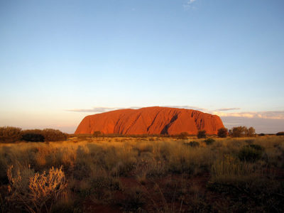 a large rock in the desert with Uluru in the background