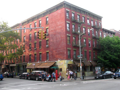 a red building with people walking on the street with Greenwich Village in the background