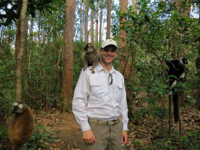 a man standing in a forest with a lemur on his shoulder