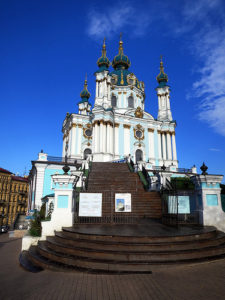 a white and blue building with a staircase with St Andrew's Church, Kiev in the background