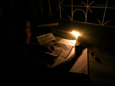 a man reading a book in a dark room with a lit candle