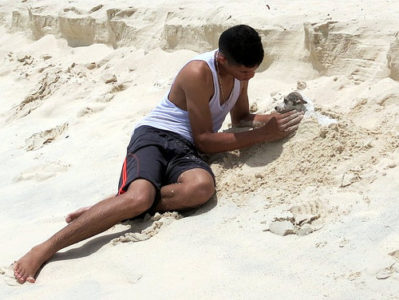 a man lying on sand with a cat